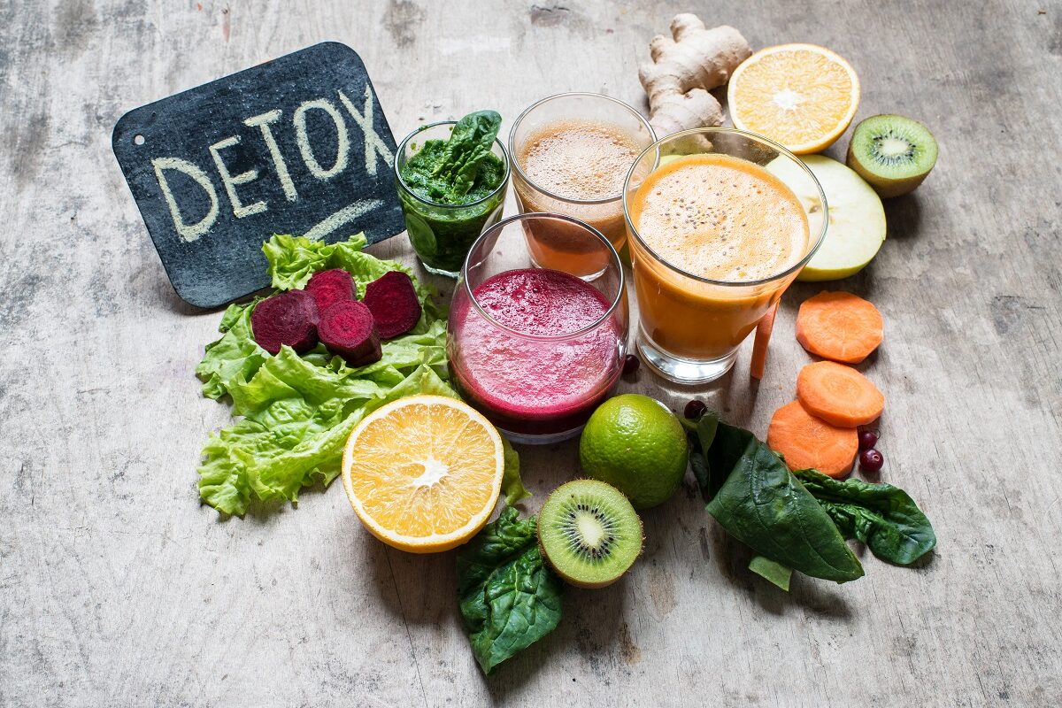 Sucuri de legume și fructe în mai multe pahare și cuvântul detox scris cu cretă pe o tablă mică, sugestiv pentru cea mai bună dietă de detoxifiere