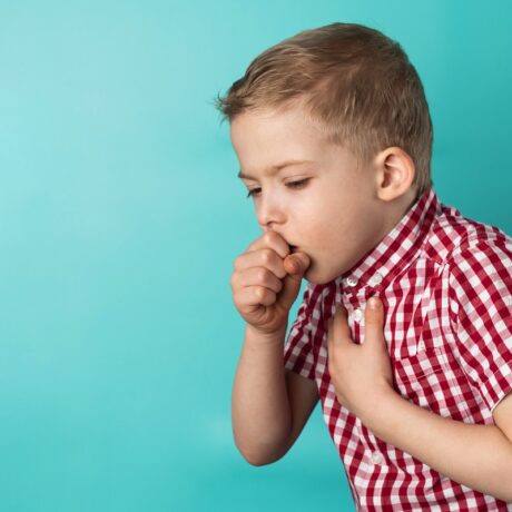 Băiat care tușește puternic cu mâna la gură, sugestiv pentru tusea convulsivă