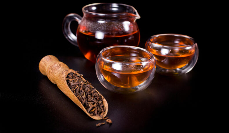 Două cești și un ceainic cu ceai Oolong, lângă o lingură cu frunze de ceai uscate