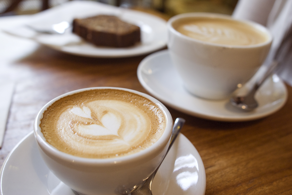 Două cești cu cafea, lângă o farfurie cu o felie de prăjitură