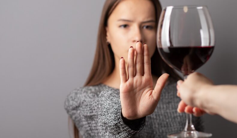 Femeie care face un semn de refuz cu mâna către un pahar de vin