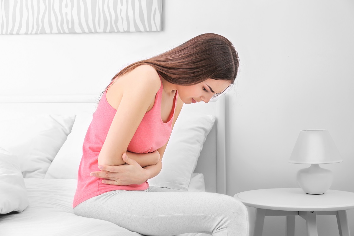 Femeie cu durere de burtă sau dureri menstruale care stă pe marginea patului și se ține de burtă, sugestiv pentru simptomele de adenomioză