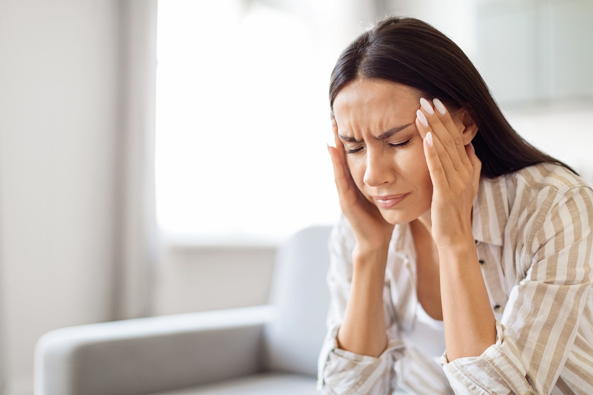 Femeie cu durere de cap care stă pe canapea, sugestiv pentru semne care anunță migrenele
