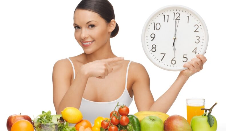 Legume și fructe în prim plan și femeie cu un ceas mare în mână care arată cu câte ore înainte de somn trebuie să mănânci