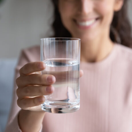 O femeie tânără zâmbește și ține un pahar cu apă