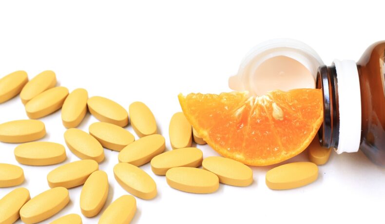 Detaliu pastile de vitamina C, o felie de portocală și o sticlă fumurie de medicamente