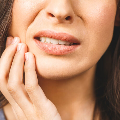 O femeie tânără își ține mâna pe maxilar din cauza unei dureri de dinți