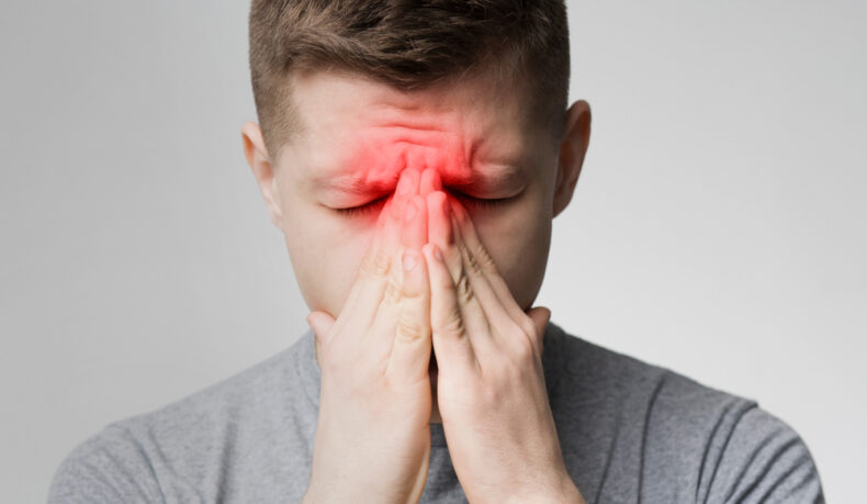 Un bărbat tânăr suferă de presiune la nivelul sinusurilor și ține mâinile la nivelul feței
