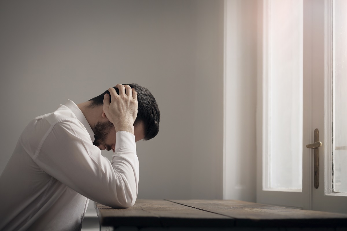 Bărbat deprimat care stă la masă cu capul între mâini, sugestiv pentru semnele depresiei la bărbați