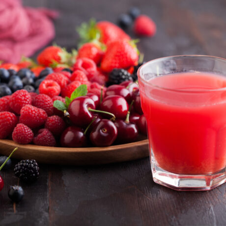 Un pahar cu suc de fructe, lângă o farfurie cu zmeură, coacăze, cireșe și mure
