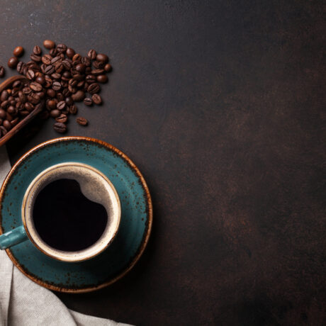 O ceașcă cu cafea, lângă o lingură cu boabe de cafea, puse pe un șervet
