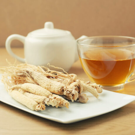 O ceașcă cu ceai de ginseng, lângă un ceainic și o farfurie cu rădăcină de ginseng