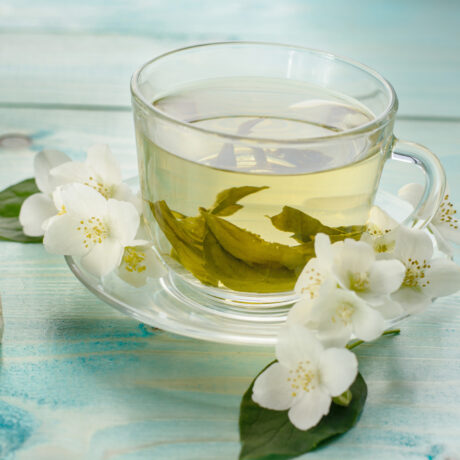 O ceașcă cu ceai alb, lângă flori de iasomie și cuburi de zahăr