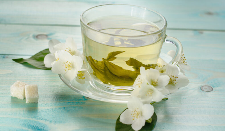 O ceașcă cu ceai alb, lângă flori de iasomie și cuburi de zahăr