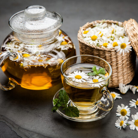 O ceașcă cu ceai de mușețel, lângă cu ceainic și un coș cu flori