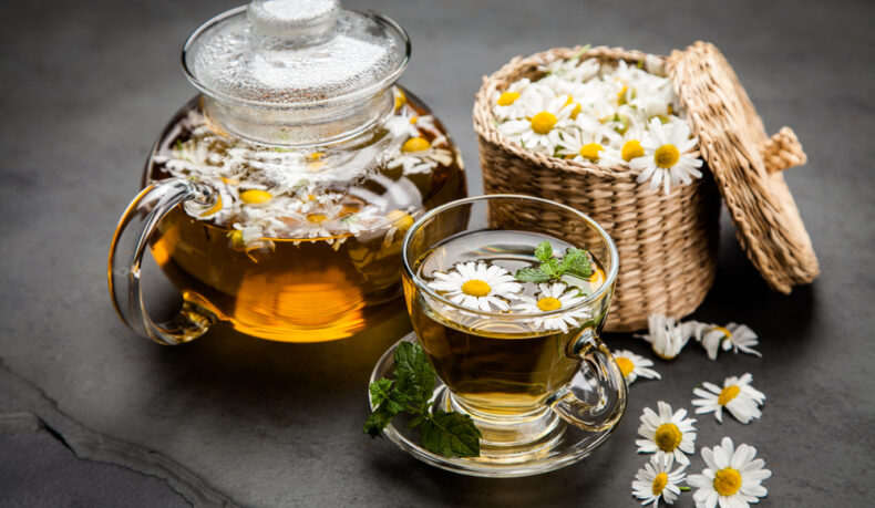 O ceașcă cu ceai de mușețel, lângă cu ceainic și un coș cu flori