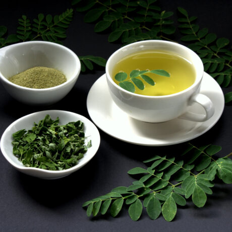 O ceașcă cu ceai de moringa, lângă două castroane cu pulbere și frunze
