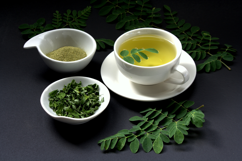 O ceașcă cu ceai de moringa, lângă două castroane cu pulbere și frunze