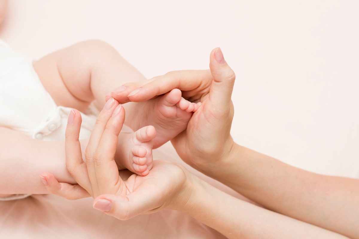 Detaliu cu picioare de bebeluș în mâinile mamei, sugestiv pentru rahitismul carențial la bebeluși