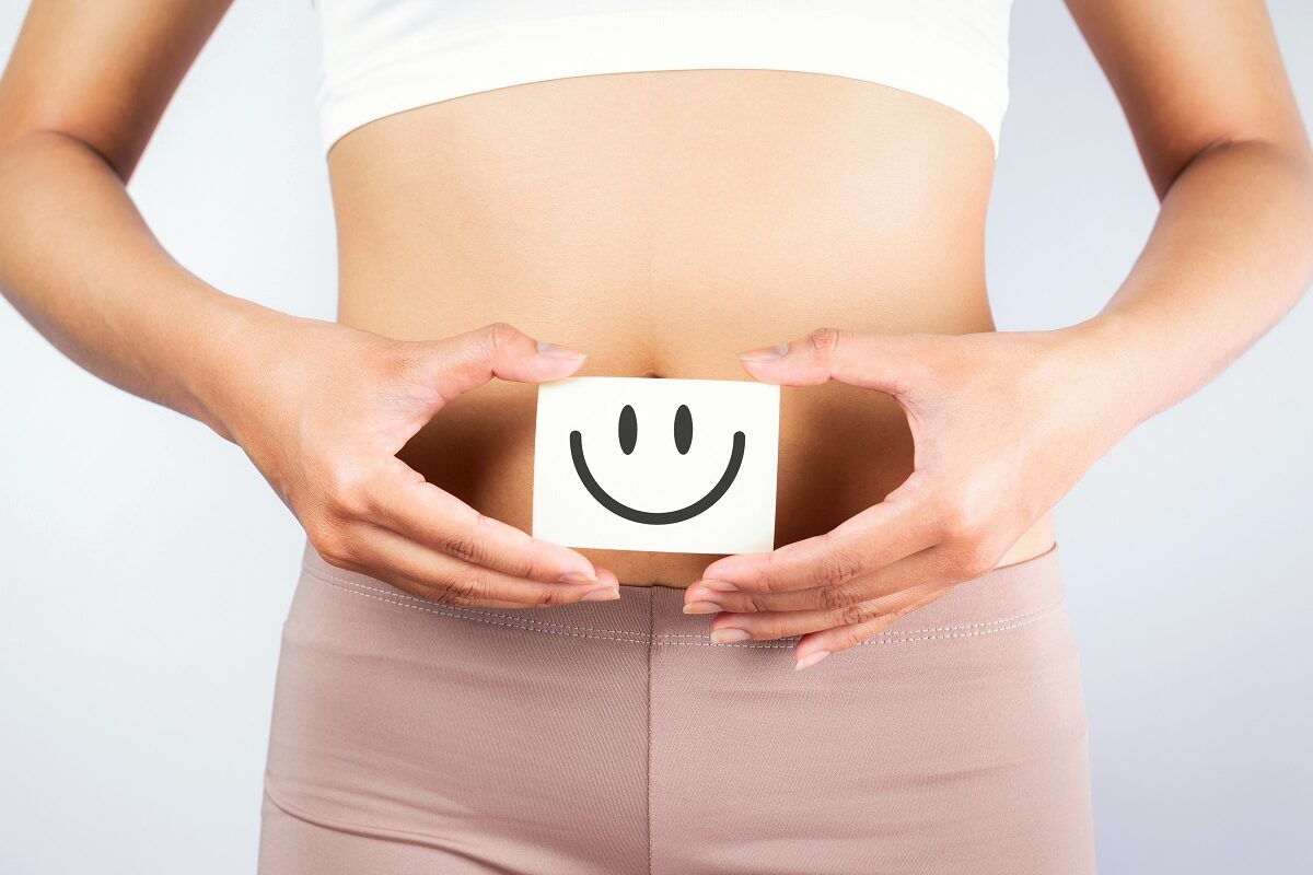 Femeie care ține un desen cu o față zâmbitoare pe burtă, sugestiv pentru sănătatea intestinală
