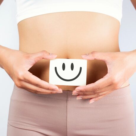 Femeie care ține un desen cu o față zâmbitoare pe burtă, sugestiv pentru sănătatea intestinală