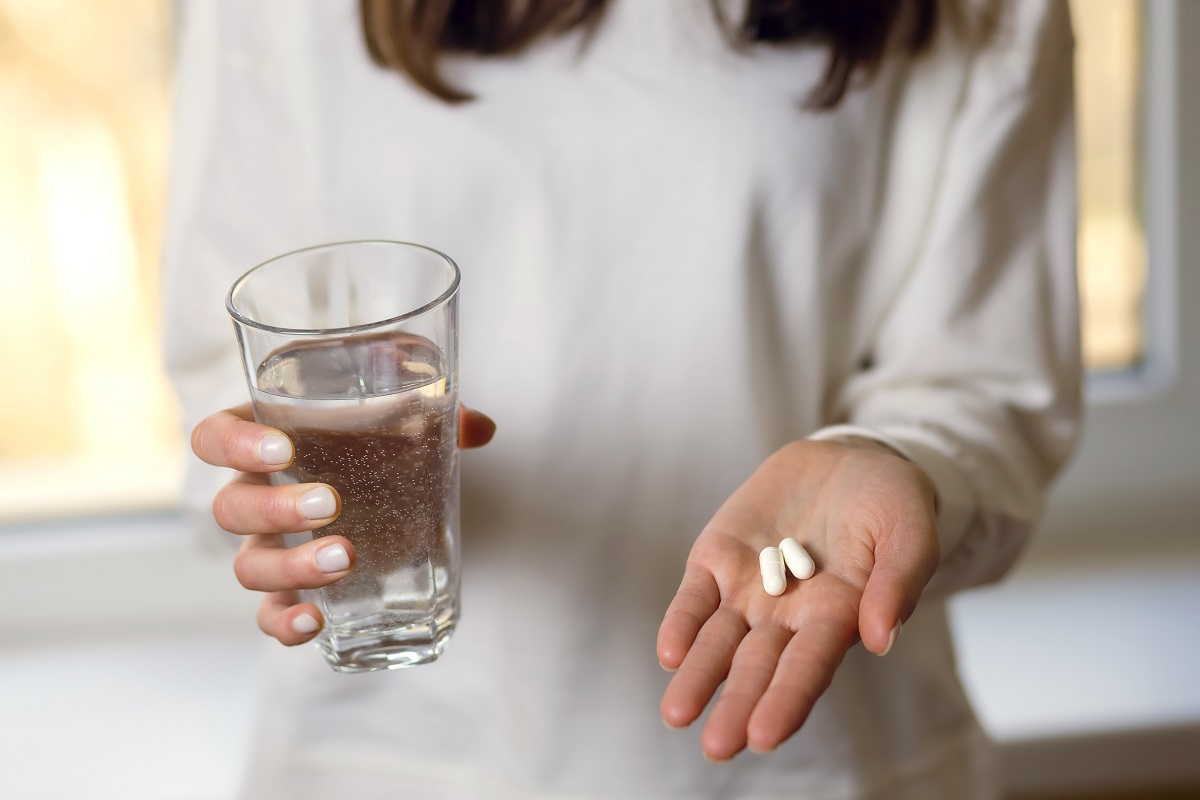 Femeie cu două pastile albe în palmă și cu pahar de apă, asemănătoare cu suplimentele cu magneziu și zinc