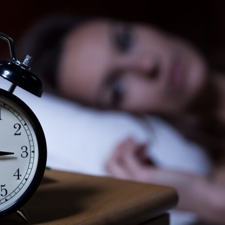 Femeie cu insomnie și ceas în fundal