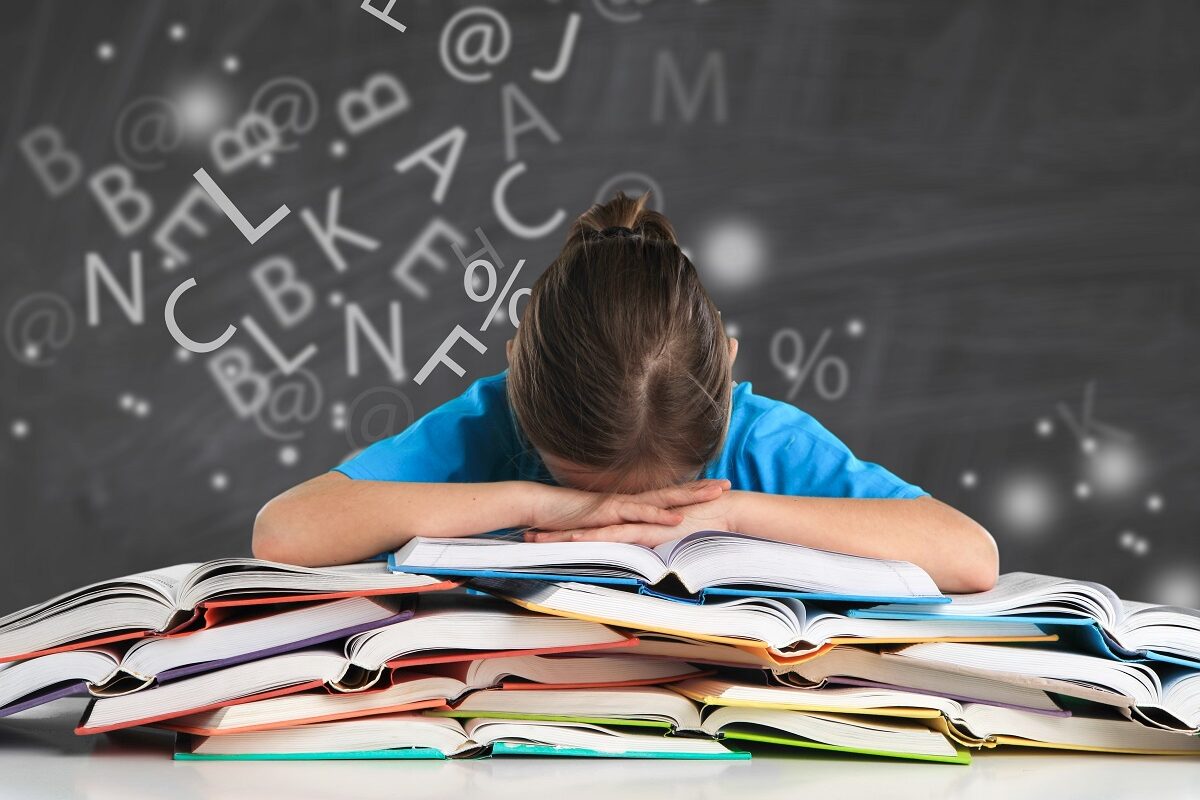 Fetiță care stă cu capul pe o stivă de cărți deschise, cu litere amestecate în jur, sugestiv pentru dificultăți la citit precum dislexia