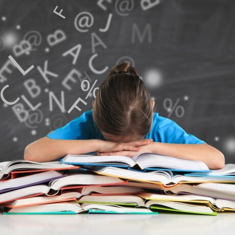 Fetiță care stă cu capul pe o stivă de cărți deschise, cu litere amestecate în jur, sugestiv pentru dificultăți la citit precum dislexia