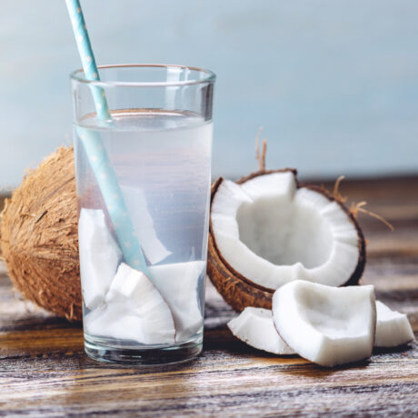 Un pahar cu apă de cocos, lângă bucăți de nucă de cocos