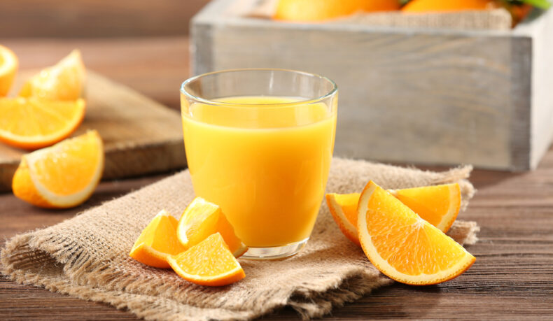 Un pahar cu suc de portocale și felii de portocale, puse pe un șervet