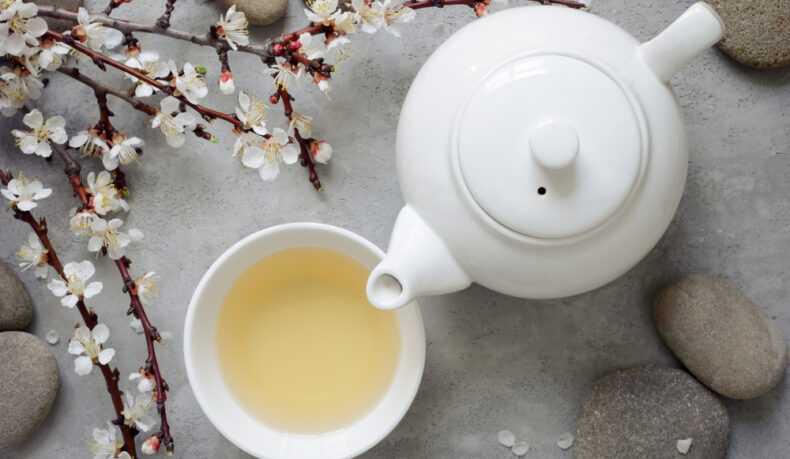 O ceașcă cu ceai alb, un ceainic și o creangă cu flori