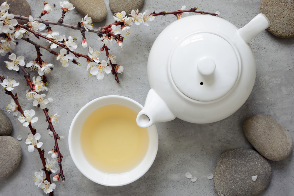 O ceașcă cu ceai alb, un ceainic și o creangă cu flori