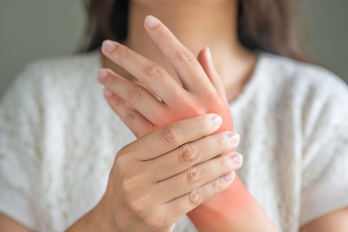 Detaliu cu mâini de femeie cu durere articulară, un simptom care apare în boala lupus