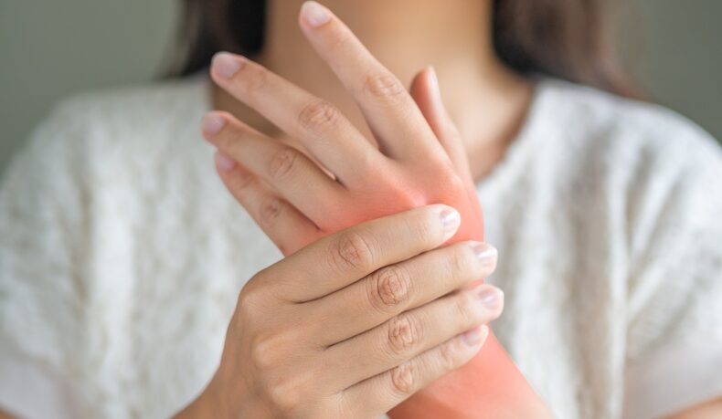 Detaliu cu mâini de femeie cu durere articulară, un simptom care apare în boala lupus