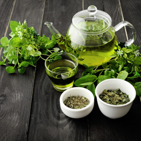 Un ceainic și un pahar cu ceai verde lângă castroane cu frunze de ceai uscate