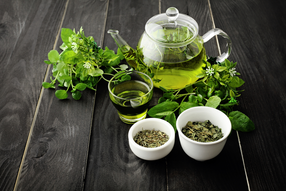 Un ceainic și un pahar cu ceai verde lângă castroane cu frunze de ceai uscate