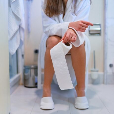 Femeie care stă pe toaletă cu hârtie igienică în mână