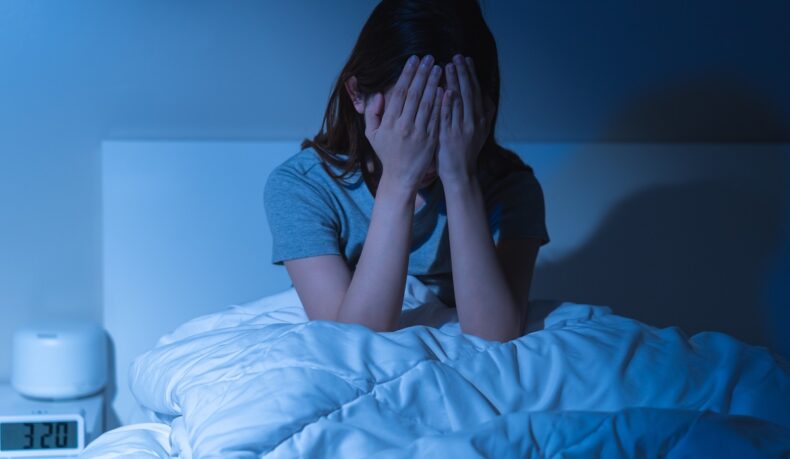 Femeie cu insomnie care stă în pat și încearcă să adormă, sugestiv pentru efectele pe care îl au nopțile nedormite asupra sănătății