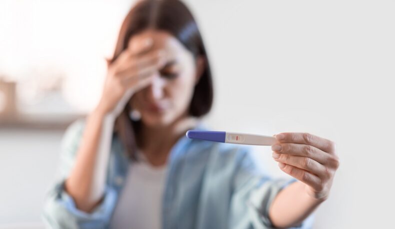 Femeie deprimată care ține în mână un test de sarcină negativ, sugestiv pentru infertilitatea cauzată de un deficit de progesteron
