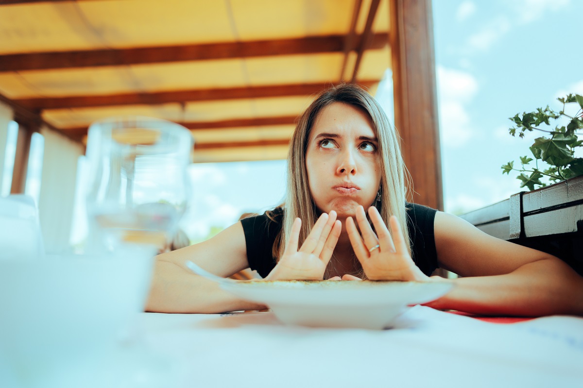 Femeie la restaurant care refuză o farfurie cu mâncare, sugestiv pentru senzația de sațietate precoce