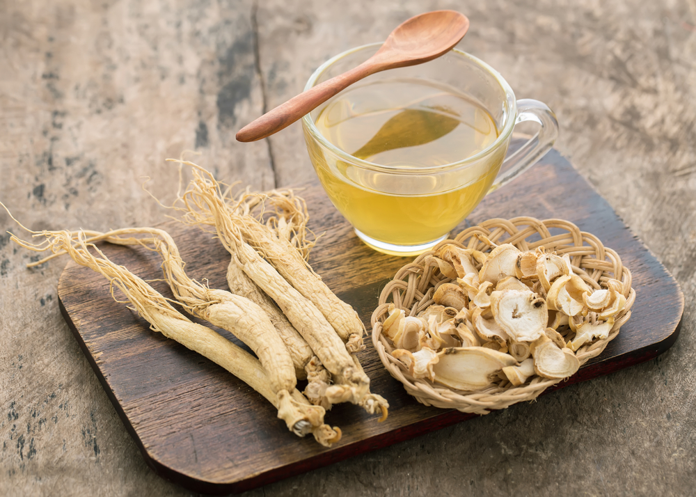 O ceașcă cu ceai de ginseng lângă bucăți de rădăcină de ginseng, puse pe un platou din lemn