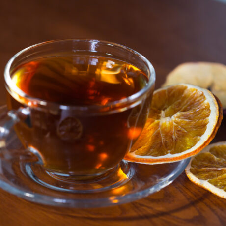 O ceașcă cu ceai de portocale pe o farfurie, lângă felii de portocale uscate