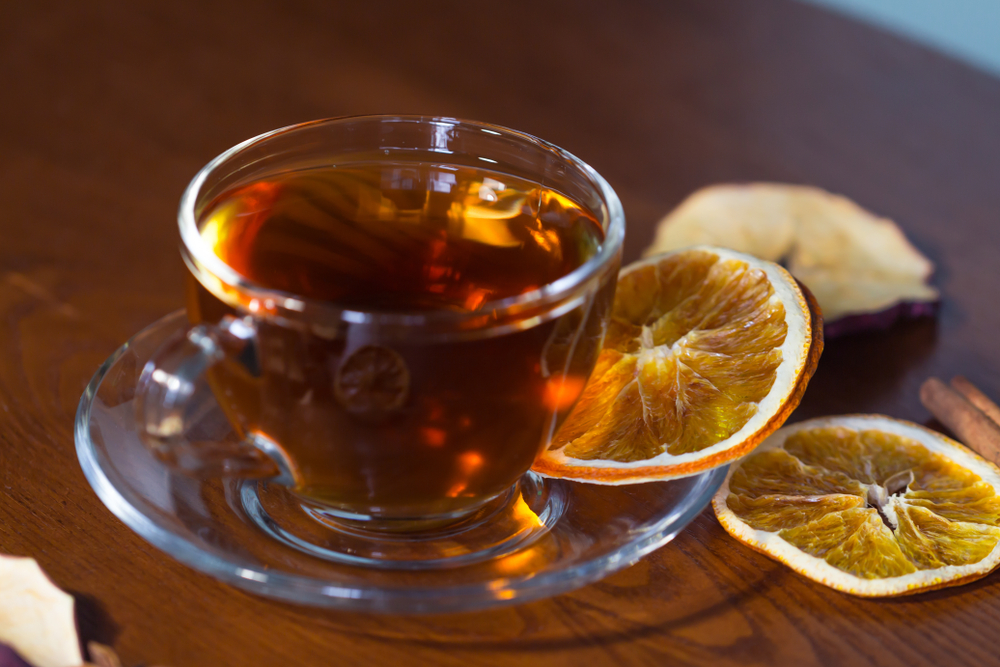O ceașcă cu ceai de portocale pe o farfurie, lângă felii de portocale uscate