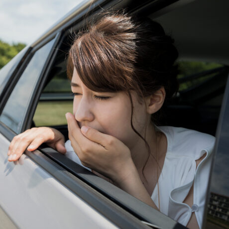 O femeie tânără ține mâna la gură la geamul unei mașini din cauza răului de mișcare