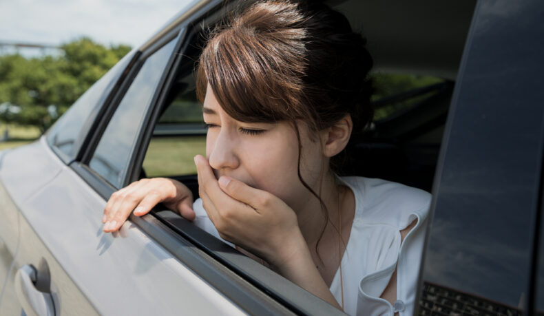 O femeie tânără ține mâna la gură la geamul unei mașini din cauza răului de mișcare