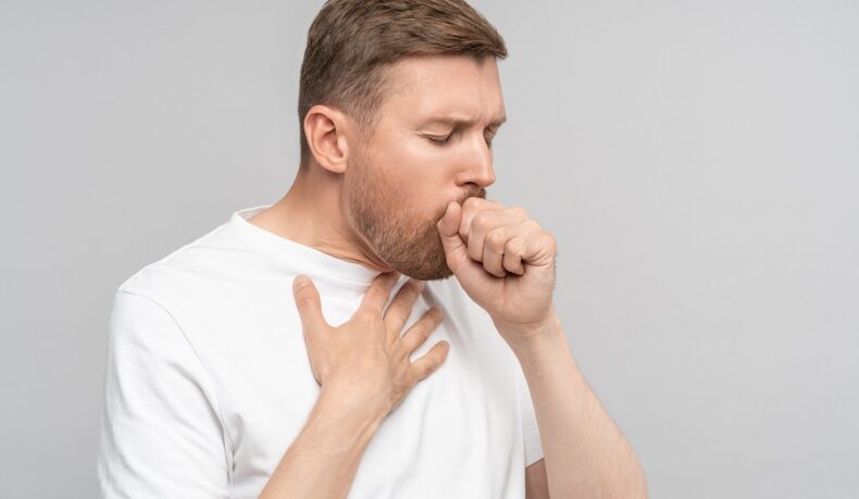 Bărbat cu mâna la gură care tușește, tusea find unul dintre simptomele cancerului pulmonar
