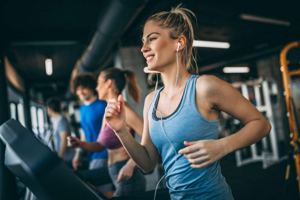 Mai multe persoane tinere care aleargă pe bandă în sala de fitness