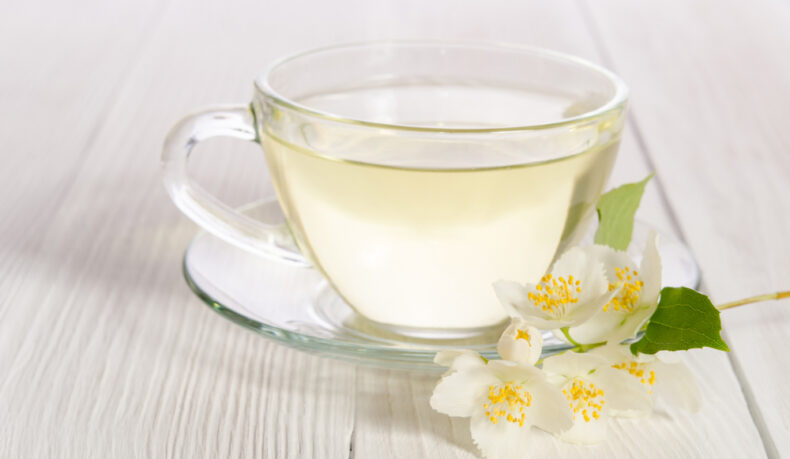 O ceașcă cu ceai alb pe o farfurie cu o floare de iasomie