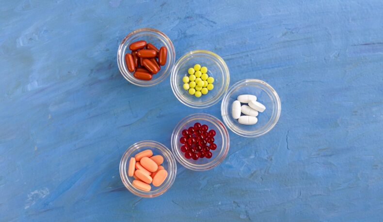 Cinci boluri cu pastile colorate pe fundal albastru, sugestiv pentru 5 suplimente care afectează rinichii